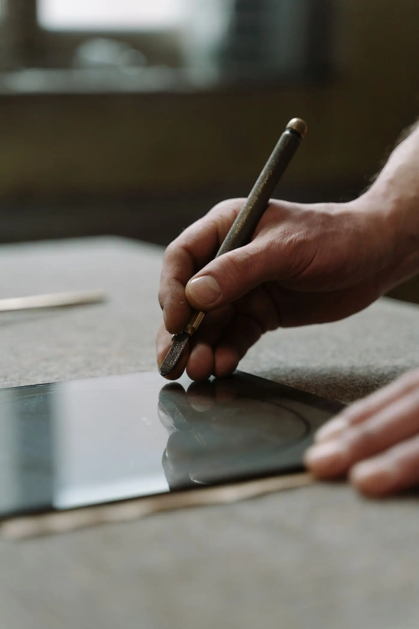 Les mains d'un vitrier qui trace au coupe-verre sur une plaque de verre