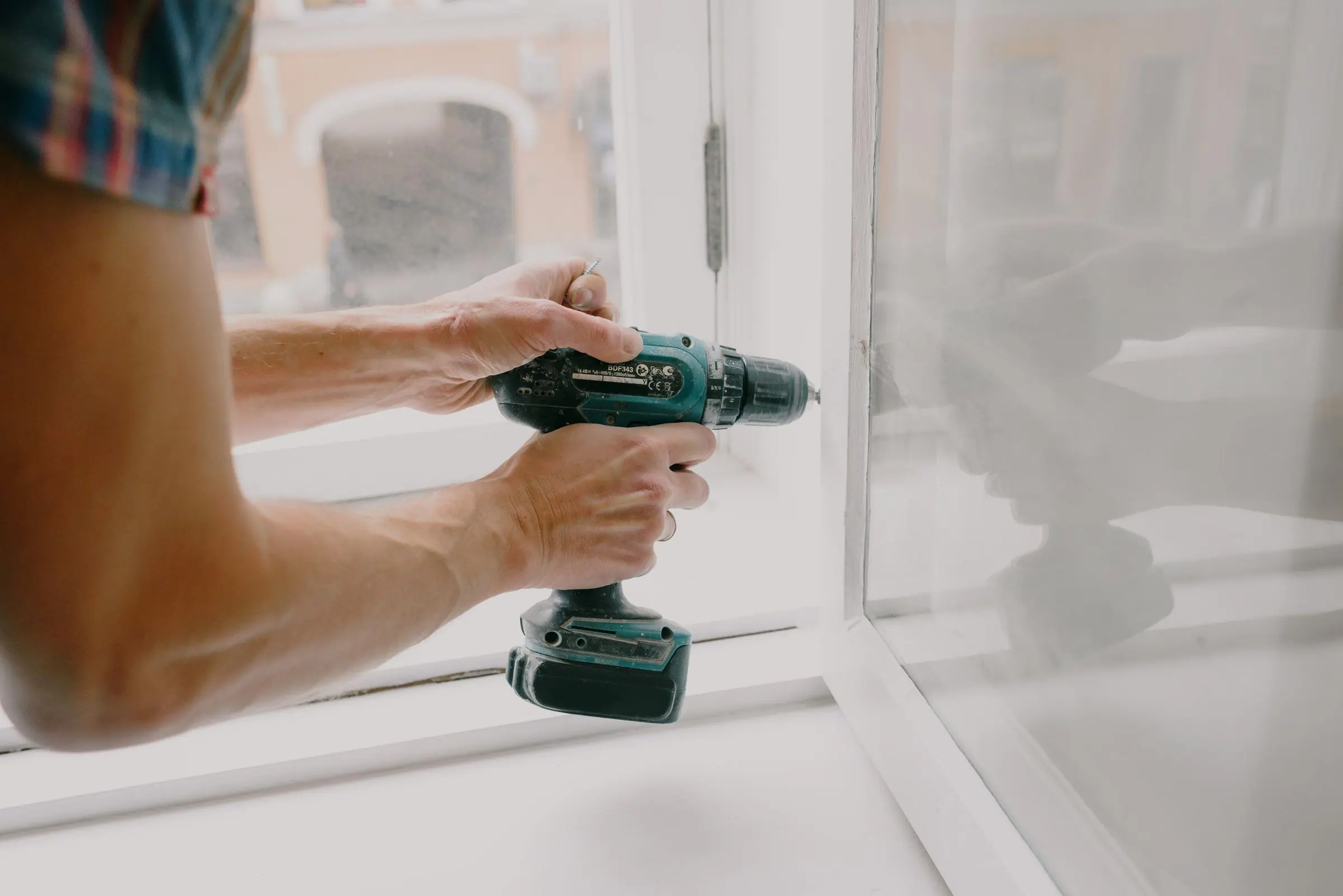Les mains d'un artisan qui fixe à la visseuse le cadre d'une fenêtre neuve