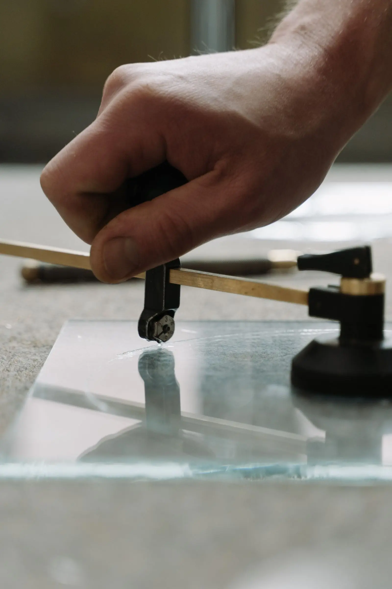 Une main guide un coupe-verre à compas sur une plaque de verre, à l'établi