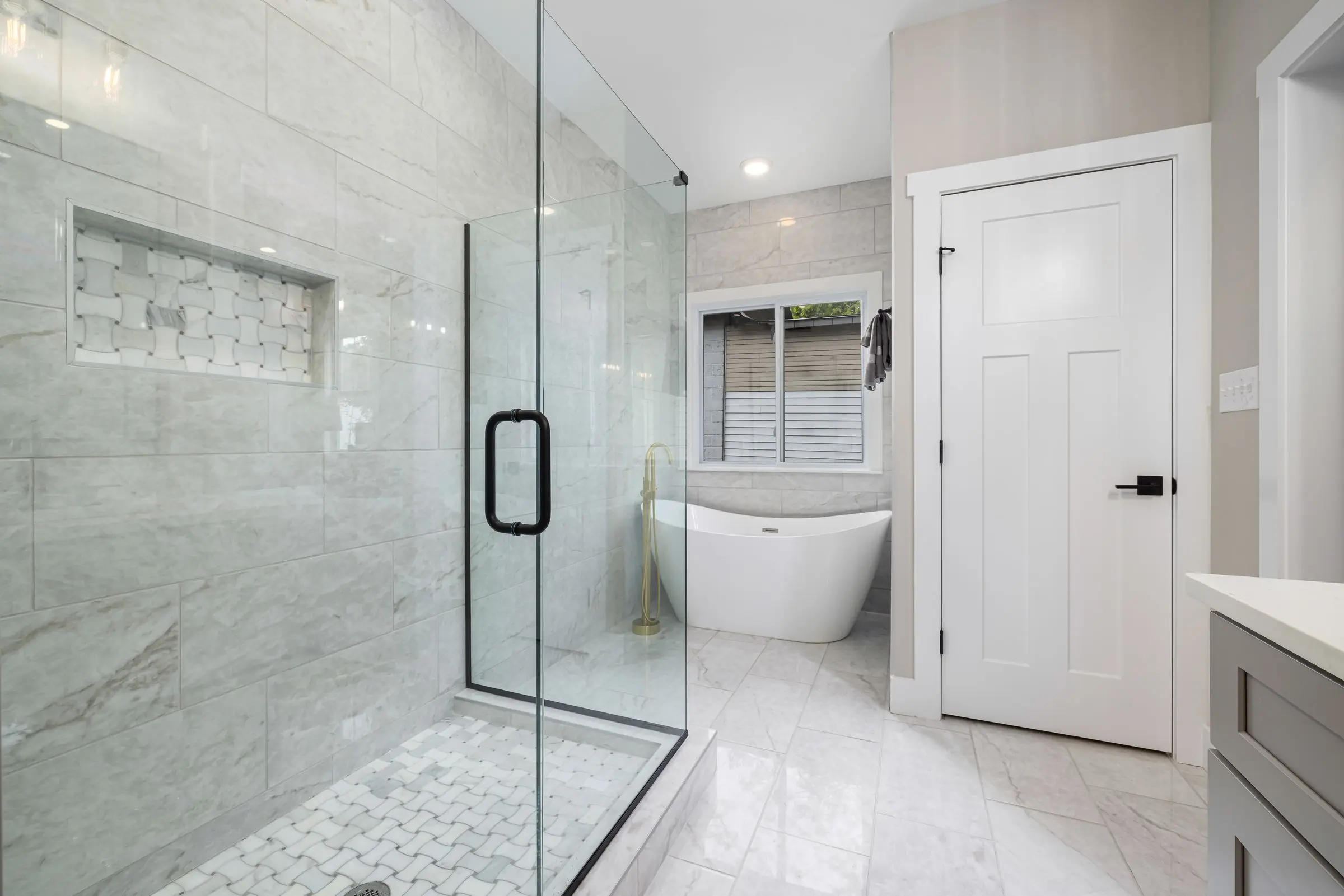 Une salle de bains claire, une grande paroi de douche en verre à la poignée noire